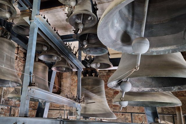 Stadtmuseum Halle Großer Glockenturm mit mehreren großen Glocken in unterschiedlichen Größen, die an Metallgestellen aufgehängt sind. Die Glocken sind teilweise mit Seilen und Mechanismen verbunden.